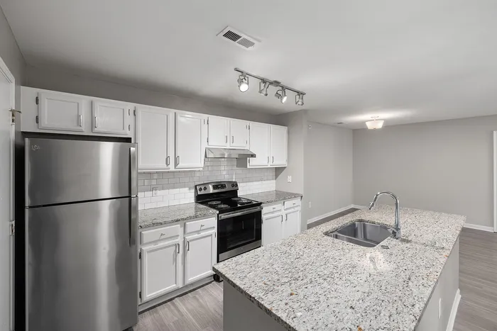 Modern kitchen featuring sleek stainless steel appliances, elegant white cabinetry, and a stylish granite countertop island with a built-in sink, ideal for contemporary living.