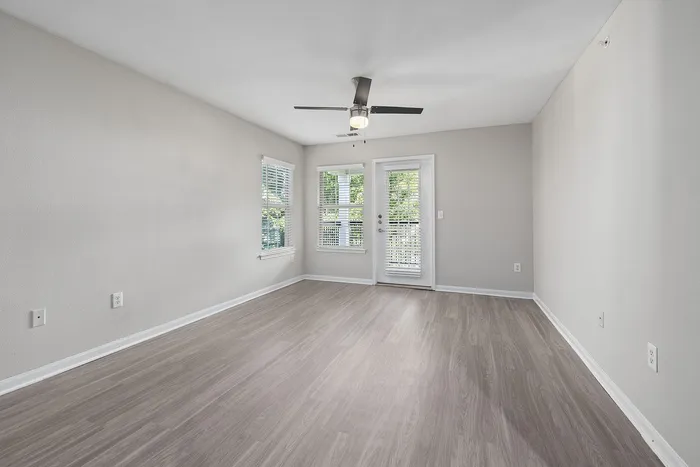 Bright and spacious living room with elegant laminate flooring, modern ceiling fan, large windows, and access to a sunlit balcony.