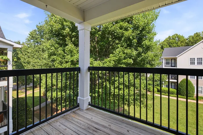Charming apartment balcony with elegant black railing, overlooking lush green trees and a beautifully maintained yard.