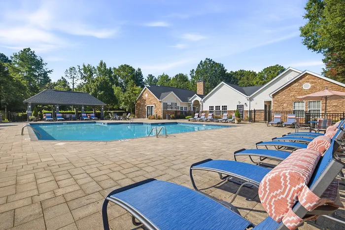 Inviting outdoor pool area with lounge chairs, surrounded by lush greenery and beautiful stone-accented clubhouse.
