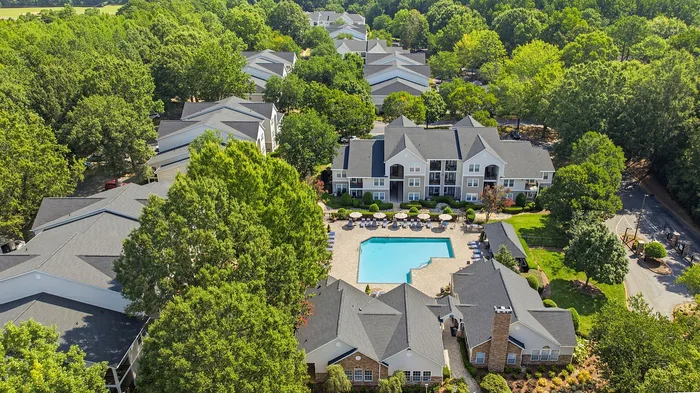 Aerial view of a picturesque apartment complex nestled in lush greenery with a sparkling central swimming pool and elegant buildings.