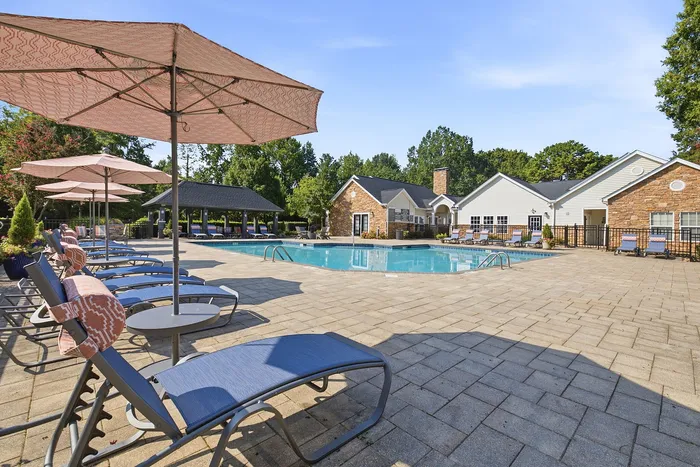 Inviting outdoor swimming pool area with elegant lounge chairs, large umbrellas, and a stylish clubhouse surrounded by lush greenery.