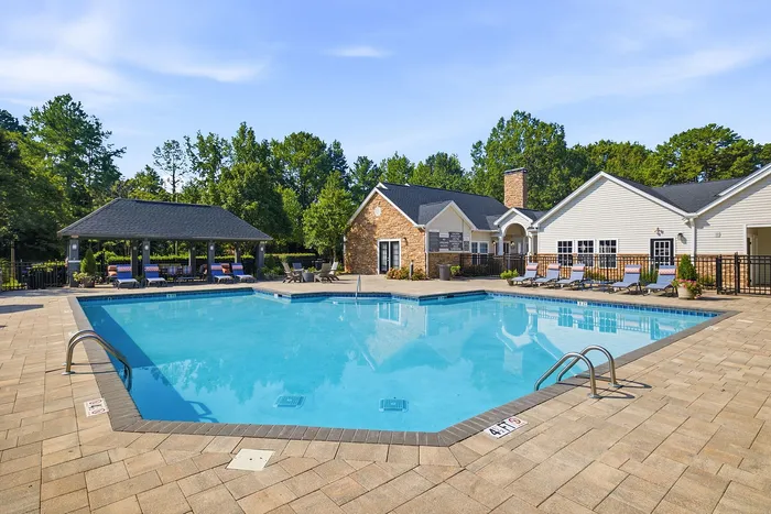 Inviting community pool area with lounge chairs, shaded seating, and lush greenery, perfect for relaxation and leisure.