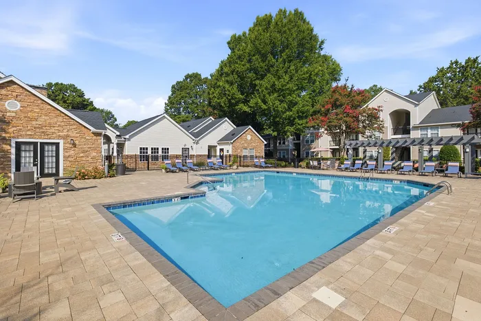 Inviting outdoor pool area with lounge chairs, surrounded by charming residential buildings and lush greenery, under a bright blue sky.
