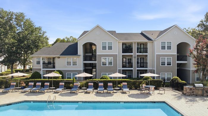 Charming apartment building featuring a beautiful outdoor swimming pool with sun loungers and umbrellas, perfect for relaxation.