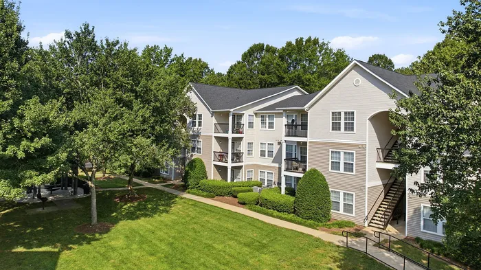 Charming apartment complex surrounded by lush trees and greenery, featuring modern exterior architecture and inviting balconies.