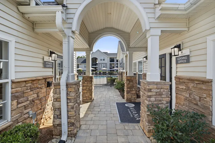 Inviting entrance to a modern apartment community showcasing elegant stone archways, fitness center, leasing office, and view of the pool area.