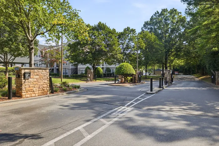 Welcoming apartment complex entrance surrounded by lush greenery and elegant stone pillars, offering a serene residential atmosphere.