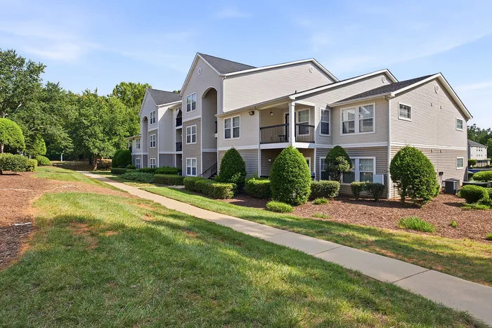 Charming apartment complex showcasing modern architecture, lush green landscaping, and a peaceful walking path.