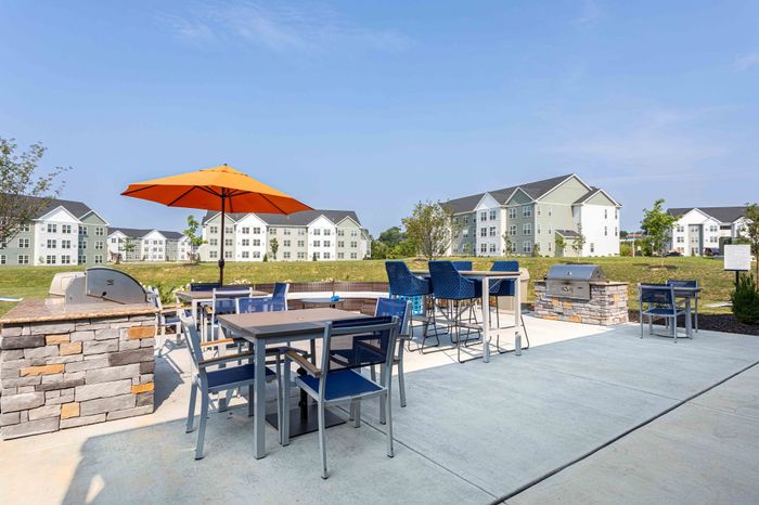 Charming apartment complex showcasing a vibrant outdoor seating area with stylish furniture and barbecue grill against a backdrop of modern buildings.