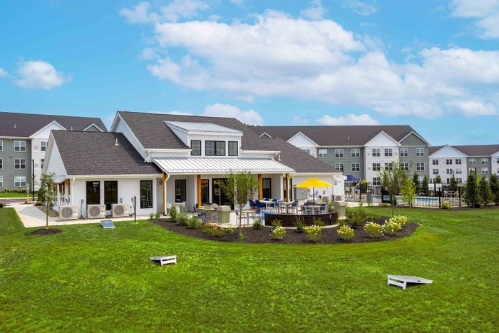 Charming suburban community with modern clubhouse, vibrant outdoor seating, lush green lawn, and sunny blue skies.