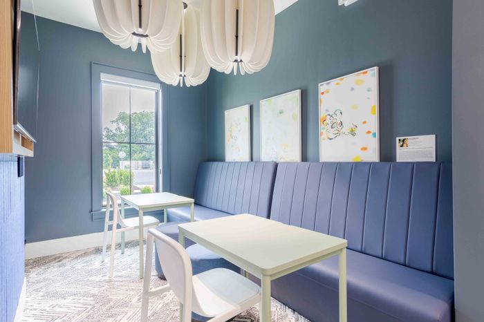 Chic dining nook with sleek blue banquette seating, modern white tables, and artistic wall decor under stylish pendant lighting.