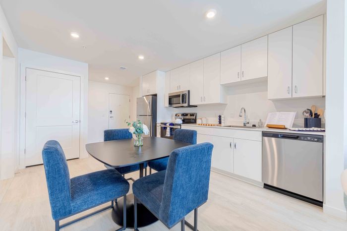 Bright and modern kitchen-dining area with sleek stainless steel appliances, elegant white cabinetry, and a cozy dining table with stylish blue chairs.