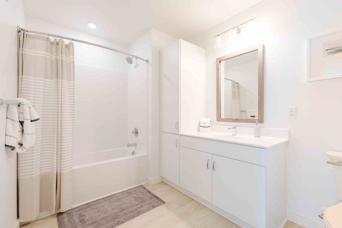 Bright and modern bathroom featuring a sleek white vanity, large mirror, and elegant shower-tub combination.