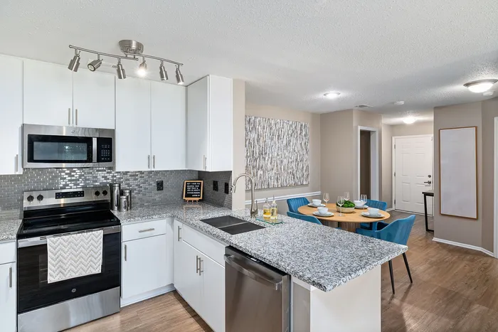 Modern kitchen and dining area featuring sleek granite countertops, stainless steel appliances, and chic dining setup with blue chairs.