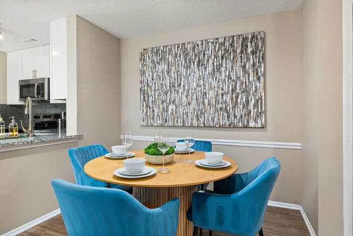 Contemporary dining area with a stylish wooden table, vibrant blue chairs, and chic artwork, adjacent to a modern kitchen.