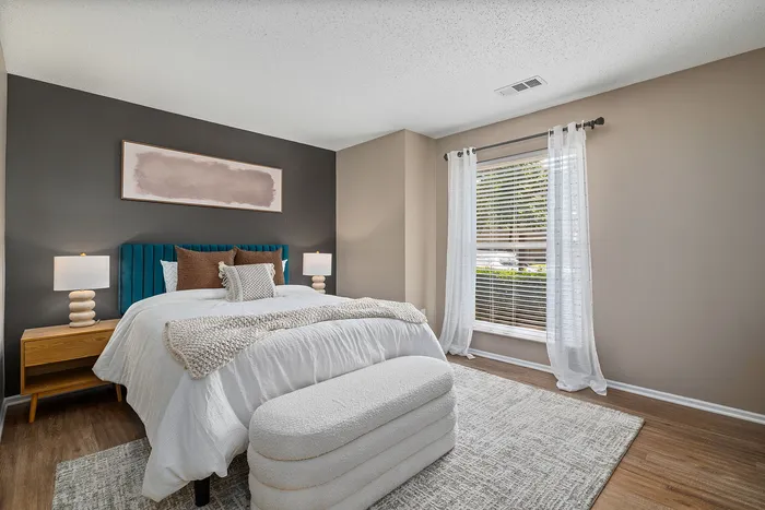 Inviting bedroom with elegant decor, featuring a plush bed, modern side tables with lamps, and a large window with natural light streaming through sheer curtains.