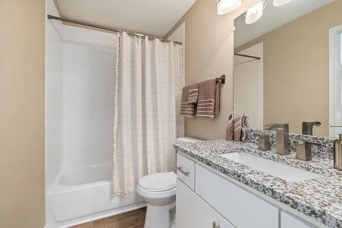 Elegant bathroom featuring a modern granite countertop, sleek fixtures, and a stylish shower with a soft curtain.