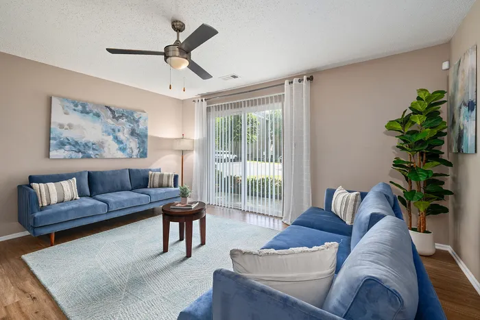 Bright and inviting living room with elegant blue sofas, abstract artwork, and natural light streaming through large patio doors, creating a serene and modern atmosphere.