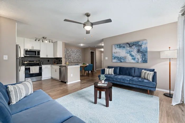 Modern open-concept apartment living room with elegant blue sofas, sleek kitchen with stainless steel appliances, and chic decor accents.