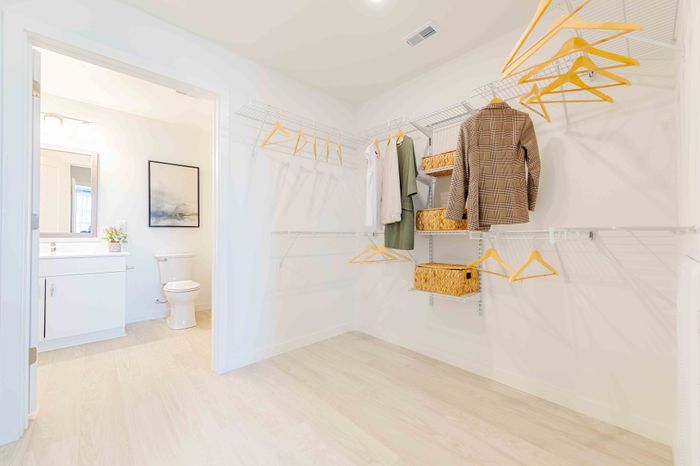 Bright and spacious walk-in closet with modern shelving, inviting light wood floors, and an adjoining sleek bathroom.