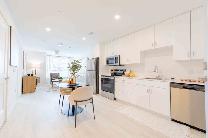 Bright and modern open-concept kitchen and dining area with sleek white cabinetry, stainless steel appliances, and natural light flooding through large windows.