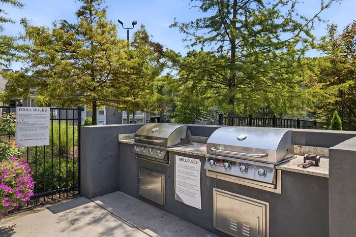 Charming outdoor grill area with modern stainless steel BBQs surrounded by lush greenery, perfect for entertaining.