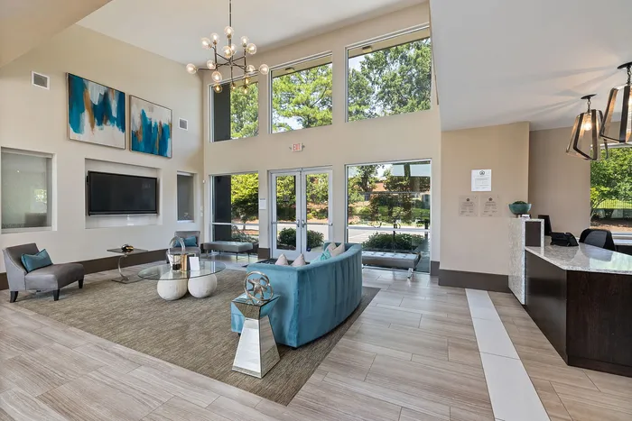 Elegant apartment lobby with modern decor, featuring a stunning chandelier, contemporary art, and plush seating areas with large windows providing ample natural light.