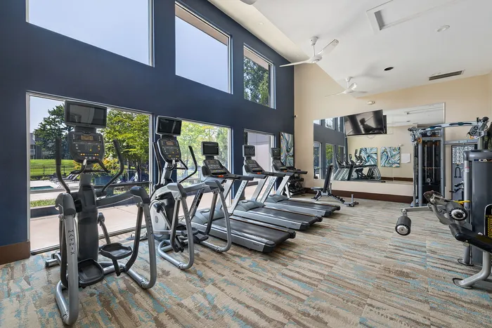 Modern fitness center with state-of-the-art equipment, including treadmills, ellipticals, and a weight machine, set against a backdrop of large windows with scenic views.
