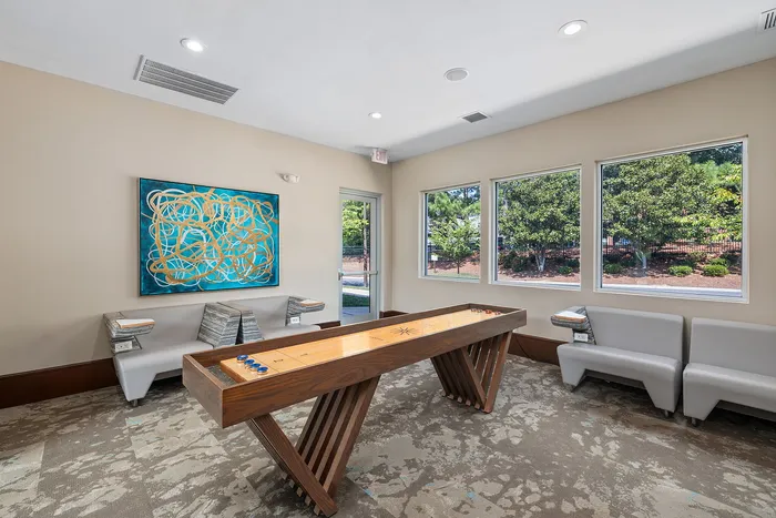 Bright and inviting recreation room featuring a modern shuffleboard table, vibrant abstract artwork, and large windows with scenic outdoor views.