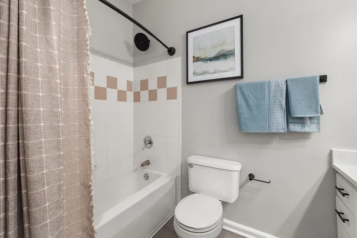Charming bathroom featuring elegant tiled shower, plush blue towels, and modern artwork on neutral walls.