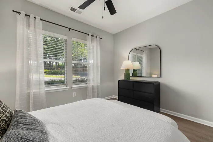 Bright, modern bedroom featuring large windows, elegant dresser with mirror, and a cozy atmosphere perfect for relaxation.