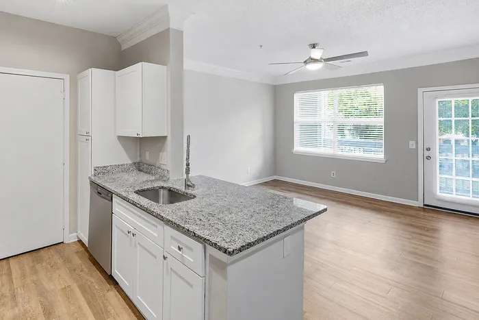 Bright, modern open-concept kitchen with sleek granite countertops, white cabinetry, and gleaming hardwood floors.