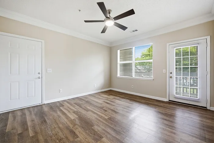 Bright and airy room featuring sleek hardwood flooring, modern ceiling fan, and expansive windows overlooking greenery.