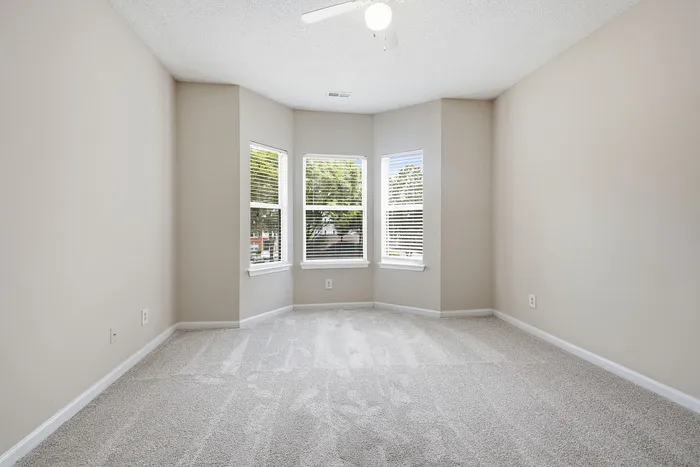 Bright and airy bedroom with plush carpet and a ceiling fan, featuring a charming bay window with outdoor views.