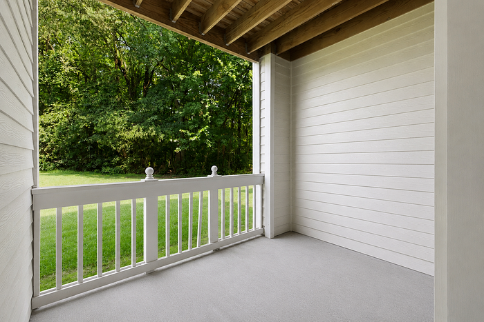 Charming covered patio with white railing overlooking lush greenery, perfect for relaxation and enjoying nature.