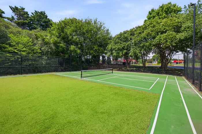 Vibrant community tennis court surrounded by lush greenery, perfect for outdoor recreation and relaxation.