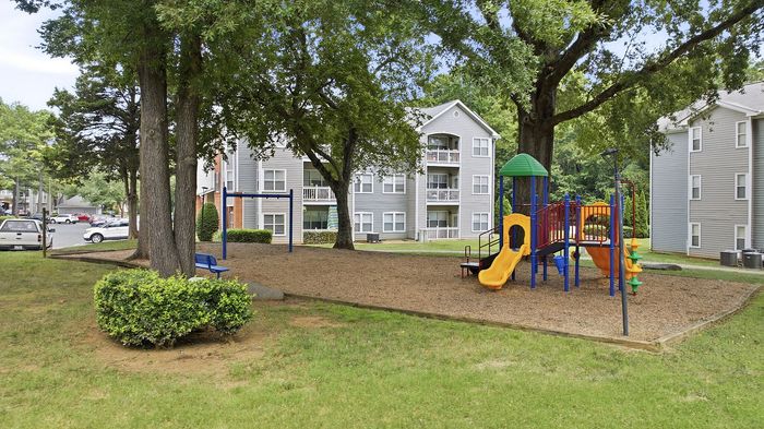 Charming apartment complex surrounded by lush greenery, featuring a colorful children's playground and inviting outdoor amenities.