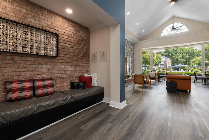 Inviting open-concept living space featuring a stylish brick accent wall, cozy seating, and expansive windows with lush garden views.
