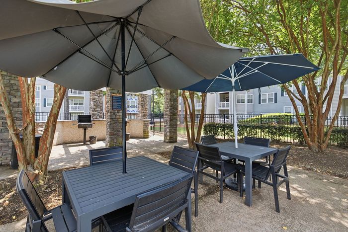 Inviting outdoor patio featuring elegant dining sets with umbrellas, nestled among lush greenery and modern apartment buildings in the background.