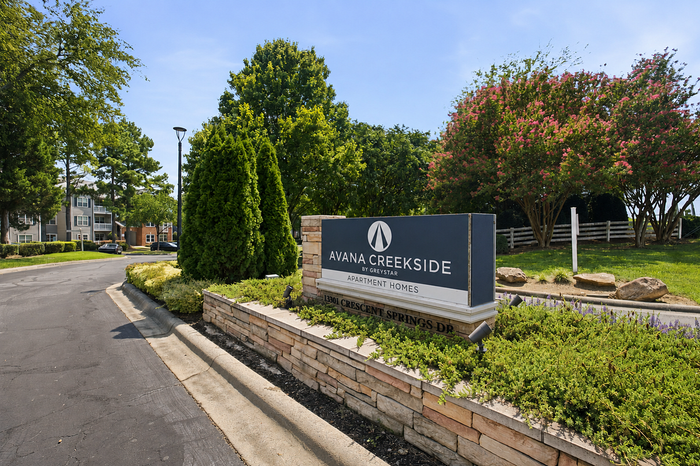 Inviting entrance to Avana Creekside Apartment Homes surrounded by lush greenery and vibrant landscaping.