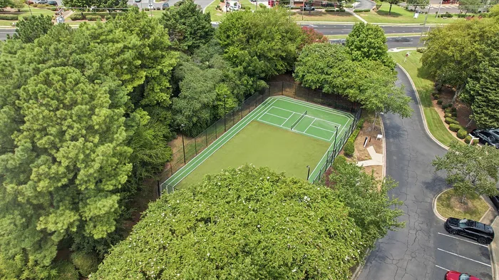 Aerial view of a beautifully maintained tennis court surrounded by lush greenery in a serene residential area.