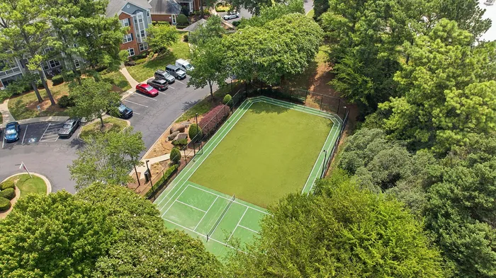 Aerial view of a vibrant apartment complex featuring lush greenery, a pristine tennis court, and ample parking space.