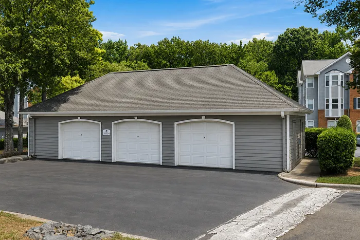 Charming residential garage with three white doors, nestled among lush greenery and modern apartments.