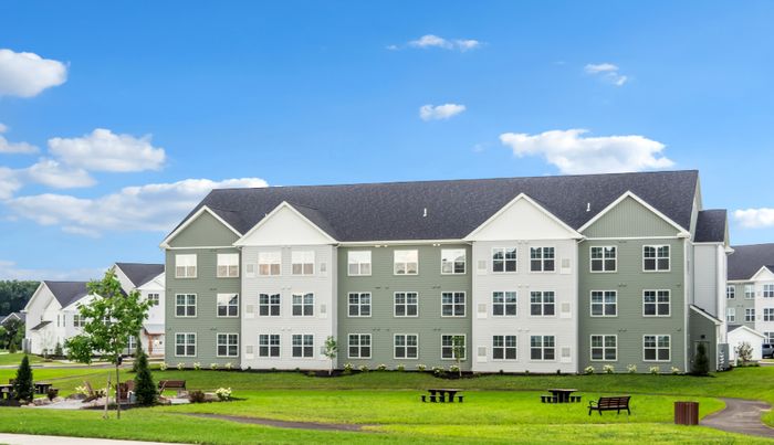 Charming green and white apartment building with modern architecture, surrounded by lush green lawns and scenic picnic areas under a clear blue sky.