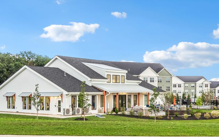 Beautiful modern apartment community with well-maintained green lawns, stylish white buildings, and inviting outdoor spaces under a clear blue sky.