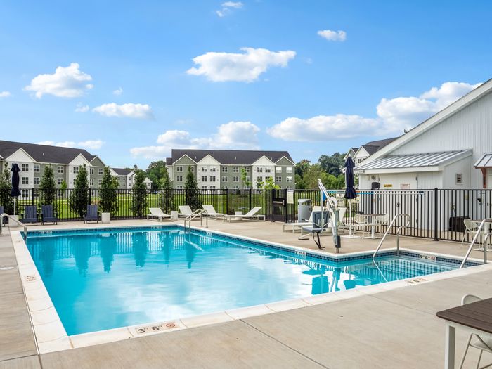 Inviting outdoor pool area with refreshing water and comfortable seating, surrounded by lush greenery and modern apartment buildings in the background.