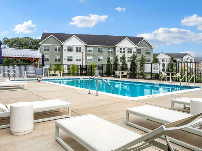 Charming apartment complex with a pristine swimming pool, surrounded by lounge chairs and a modern community patio.