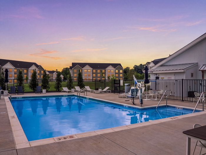 Charming apartment complex featuring a pristine swimming pool surrounded by modern lounge chairs, perfect for sunset relaxation.