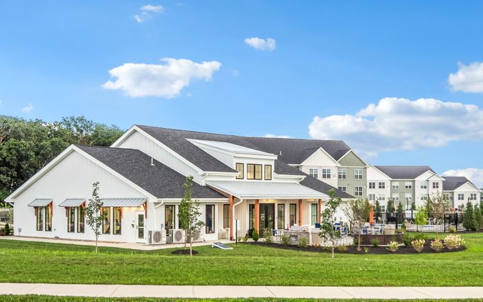 Charming clubhouse exterior with a fresh modern design, surrounded by lush green landscaping under a bright blue sky.
